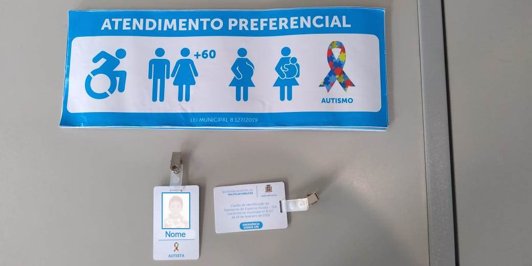 Cartões de identificação contam com foto, nome completo na frente e informações sobre a Lei Ordinária nº 8.127 no verso. Adesivos já contam com símbolo de autistas para atendimento prioritário